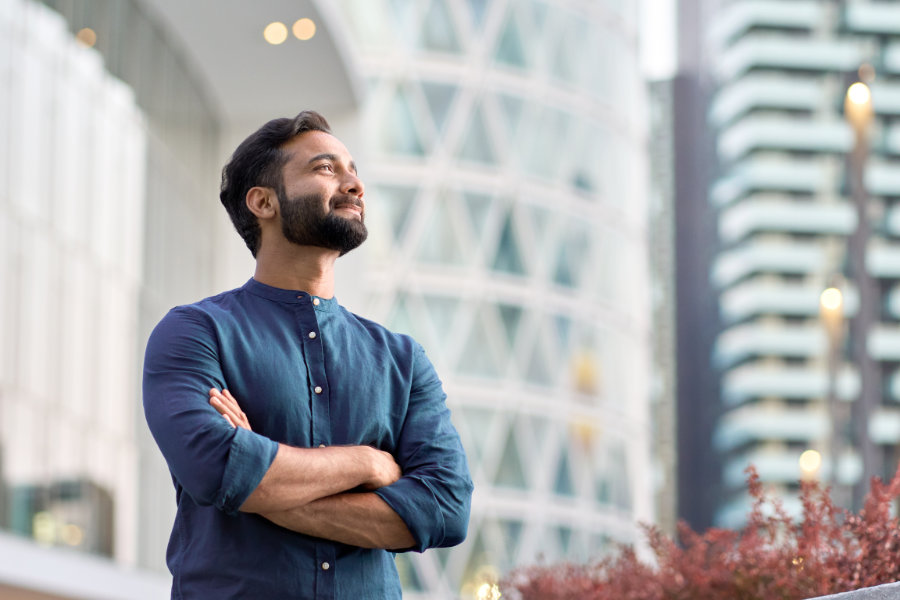 Confident rich indian business man standing in city dreaming of success.